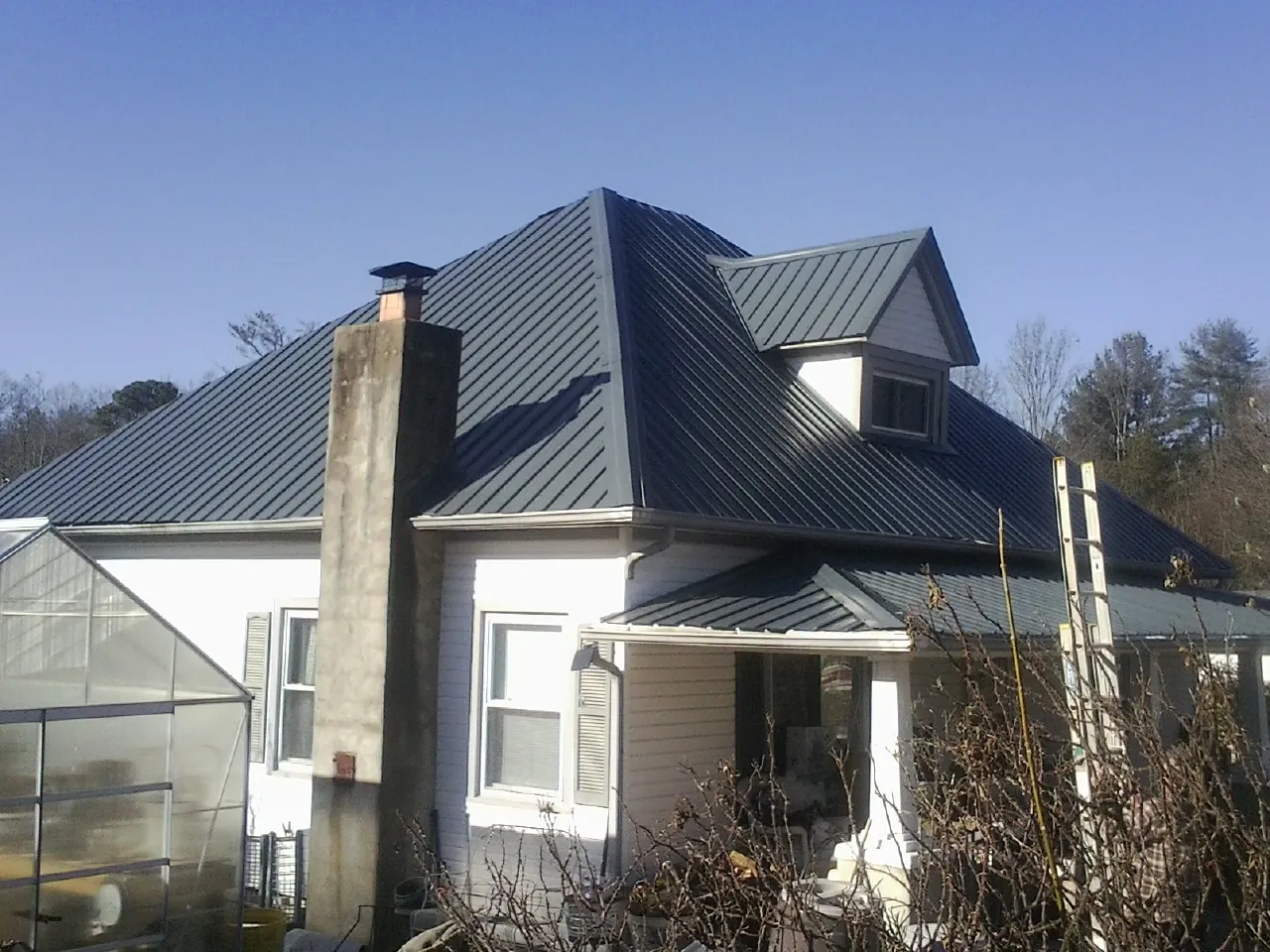 Dark blue standing seam metal roof on a white farmhouse with dormer — Slate & Tile Roof Repair by Roofing Brothers in Hacienda Heights