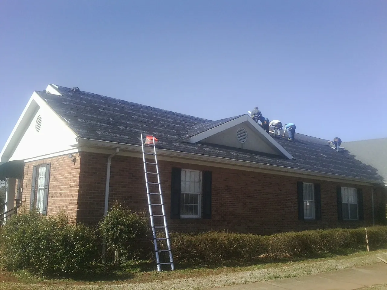 Crew tearing shingles off a brick ranch roof with a ladder set — Emergency Roof Repair work by our crew in Hacienda Heights
