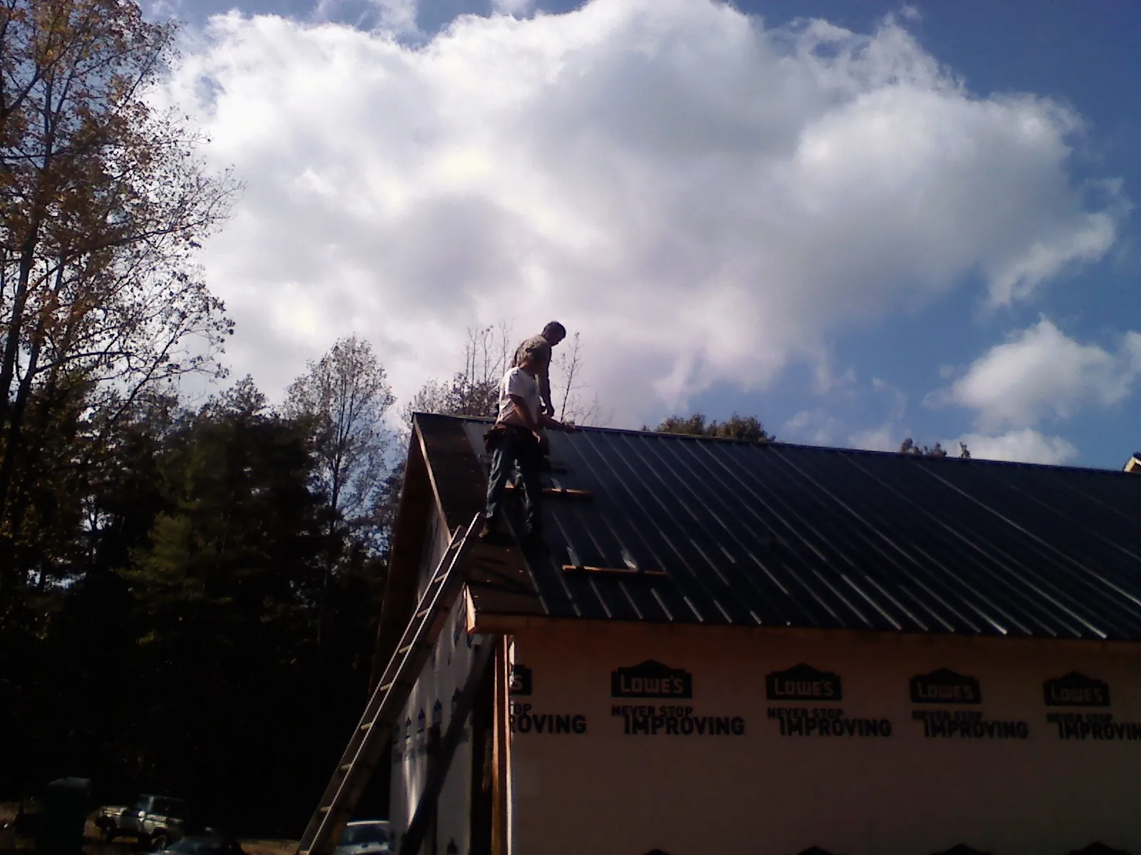 Roofer fastening dark metal panels high against a cloudy sky, from a Roof Inspection job in Hacienda Heights