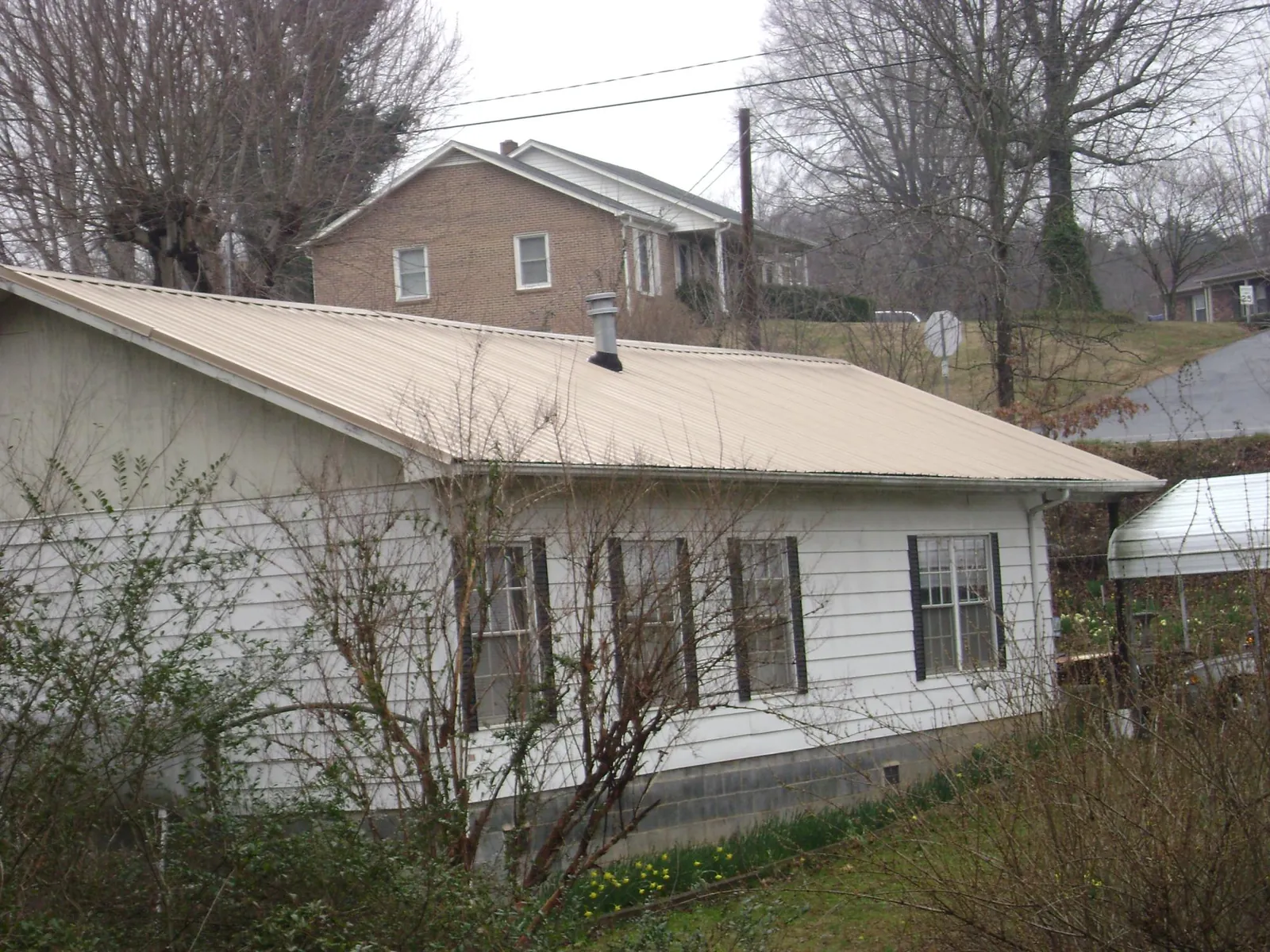 Tan metal roof on a white sided house set into a hillside — Commercial Roofing by Roofing Brothers in Hacienda Heights